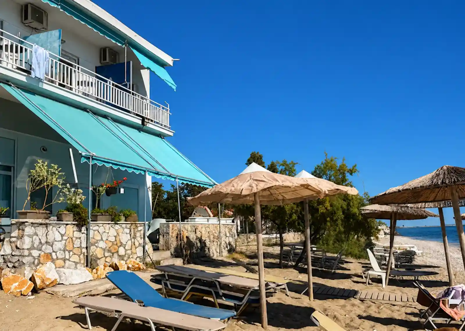 Maria Apartments seen from the sand, with awnings, sun loungers and straw parasols beside the sea in Néa Karváli