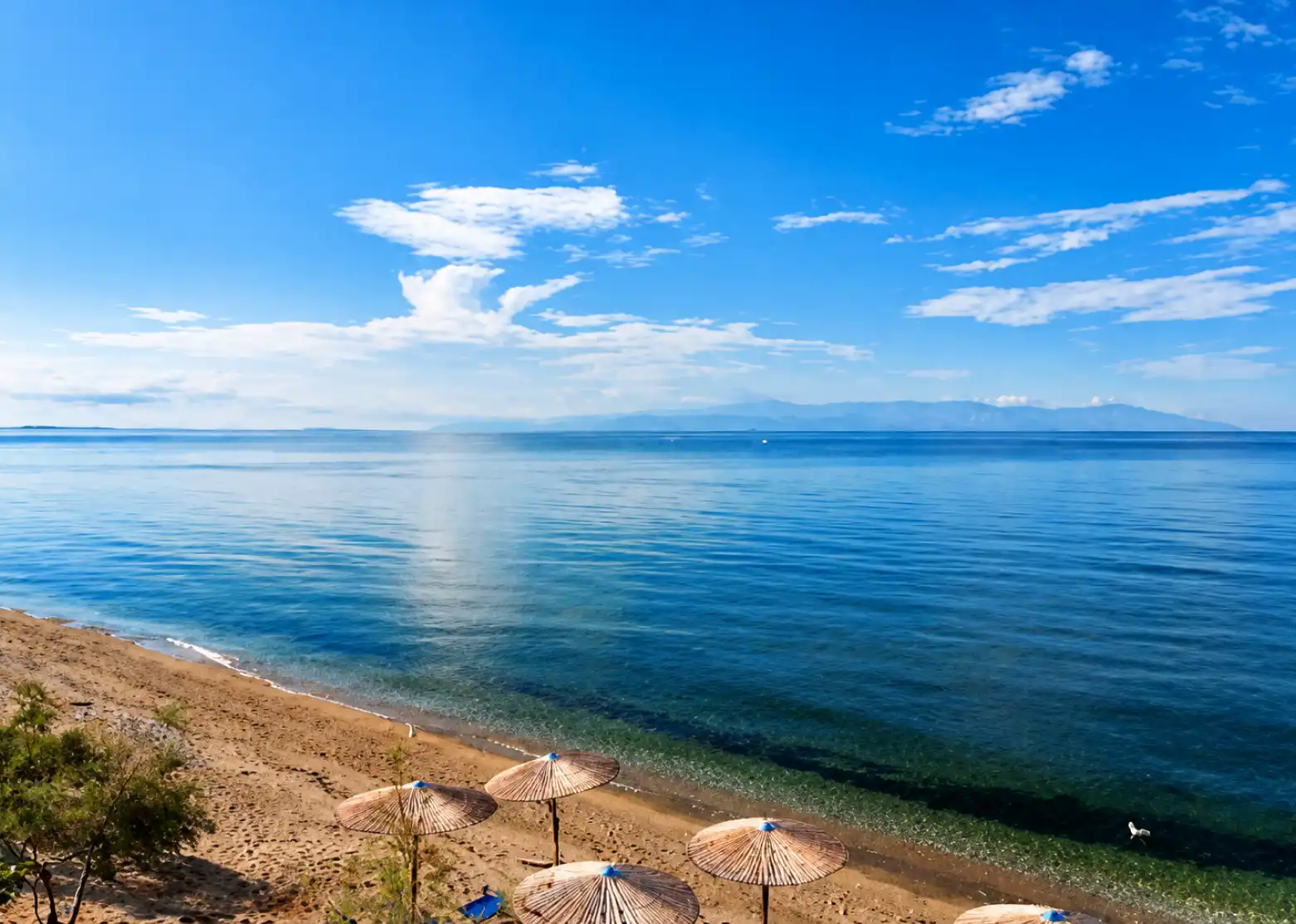 Calm Aegean shoreline at Nea Karvali Beach with straw parasols on the sand